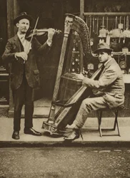 Gatumusikanter: en harpist och violinist (sepiafoto)